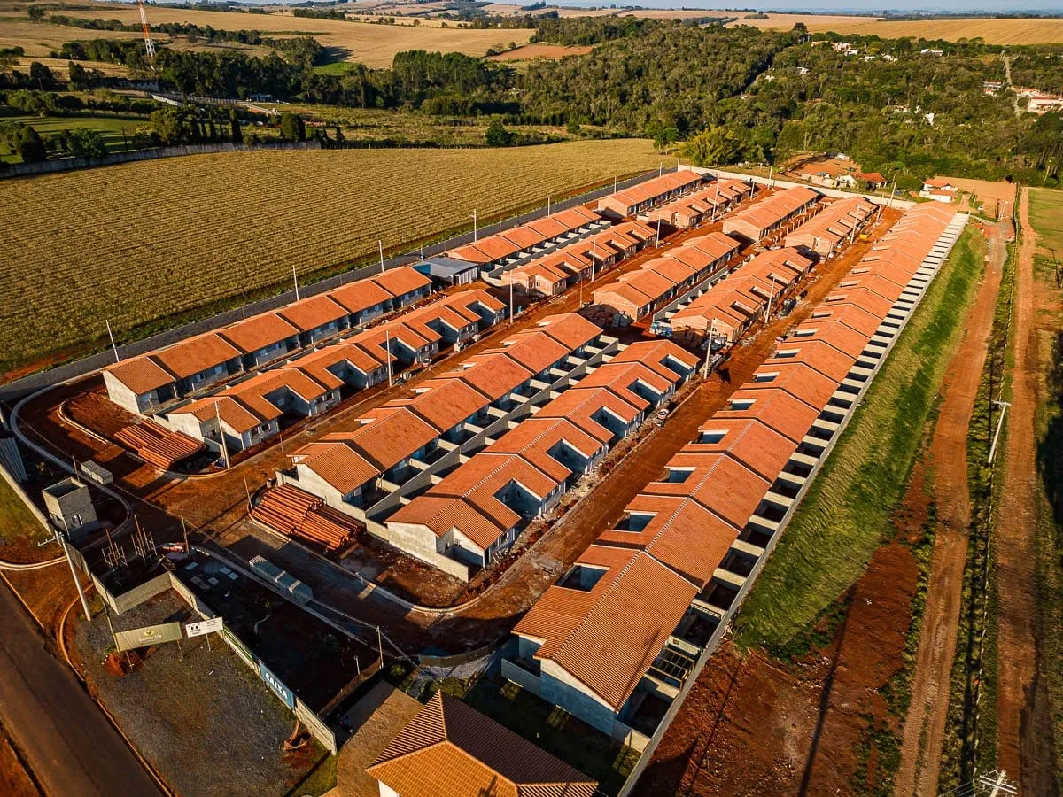 Vista aérea das fileiras de casas do Quality Life Itapê, com áreas de plantio ao redor