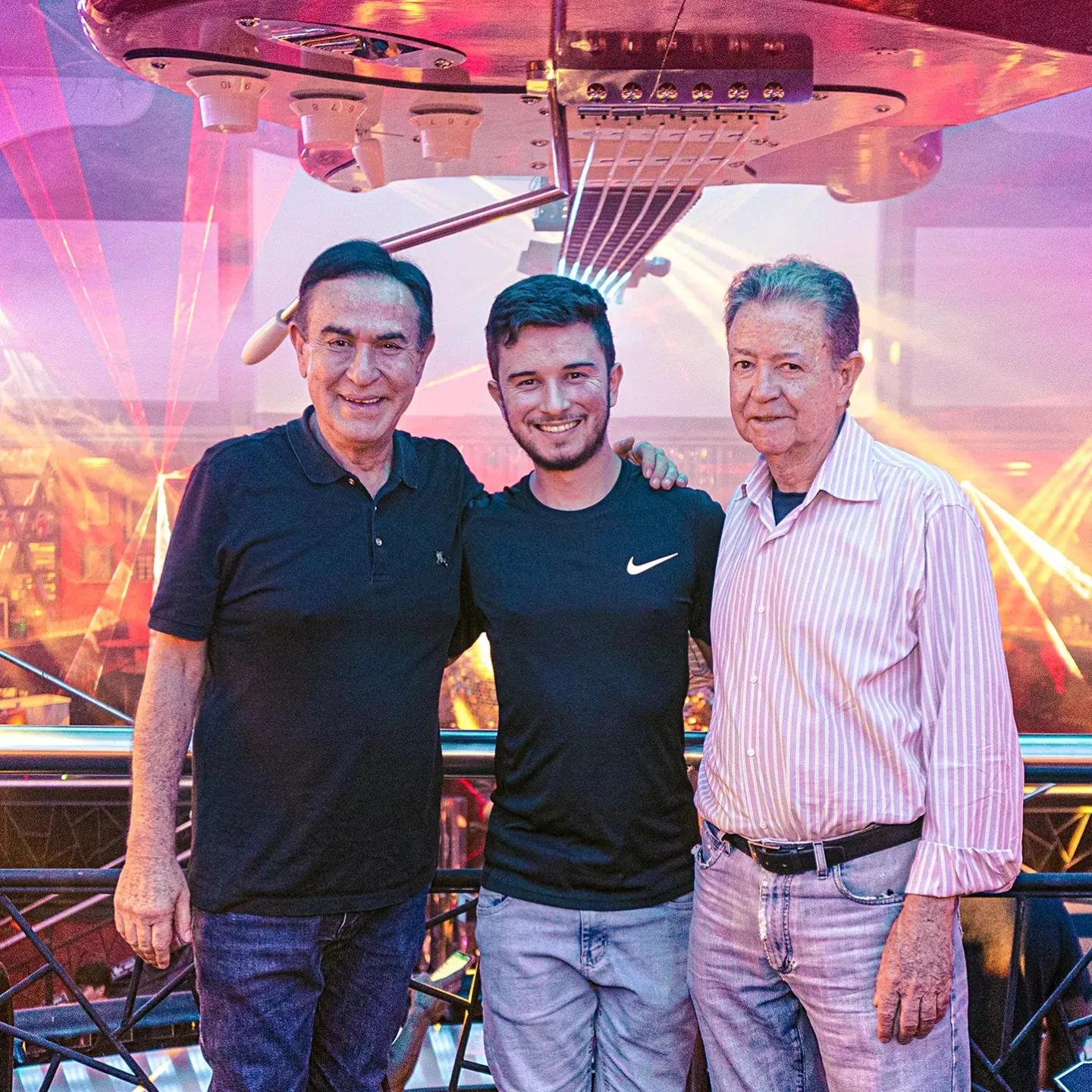 Da esquerda para a direita, Amaury Jr., Gustavo Moraes Augusto, fundador da gm360, e J.D'Avila, dono da Limelight, lado a lado no mezanino da casa, em São Paulo, embaixo da guitarra gigante do teto, com os lasers da pista ao fundo