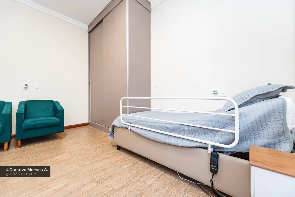 Cama automatizada com grade lateral e controle, ao lado de poltronas verdes