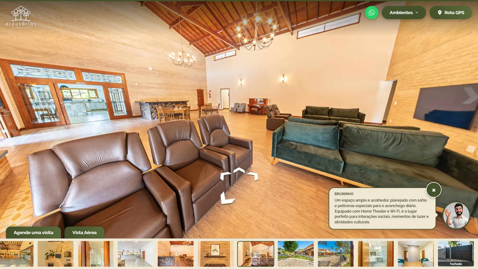 Sala de convivência com poltronas reclináveis de couro, sofás verdes e piano ao fundo, com o avatar do Bruninho e o balão sobre o espaço