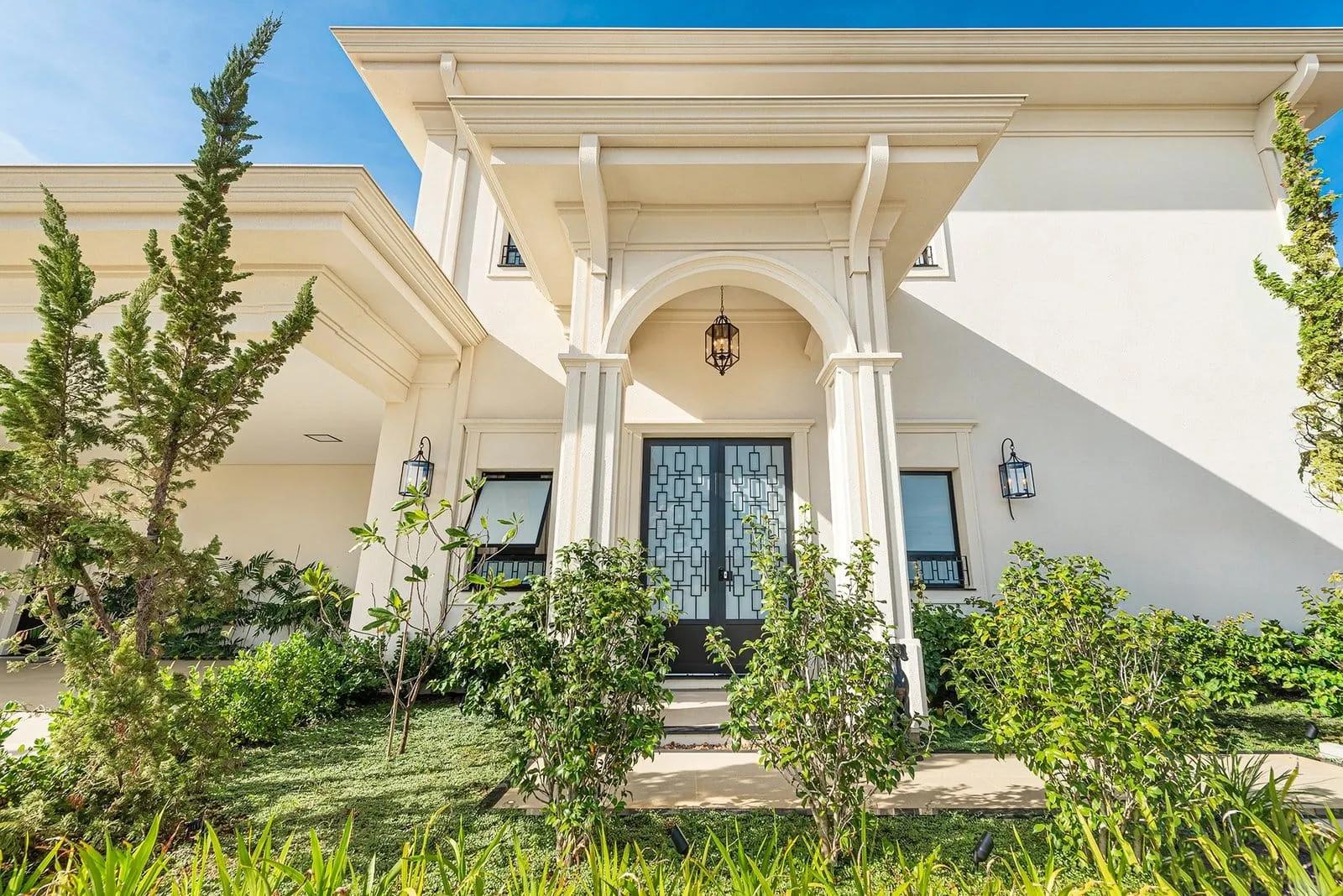 Entrada de casa branca de linhas clássicas, com colunas, porta de ferro e jardim