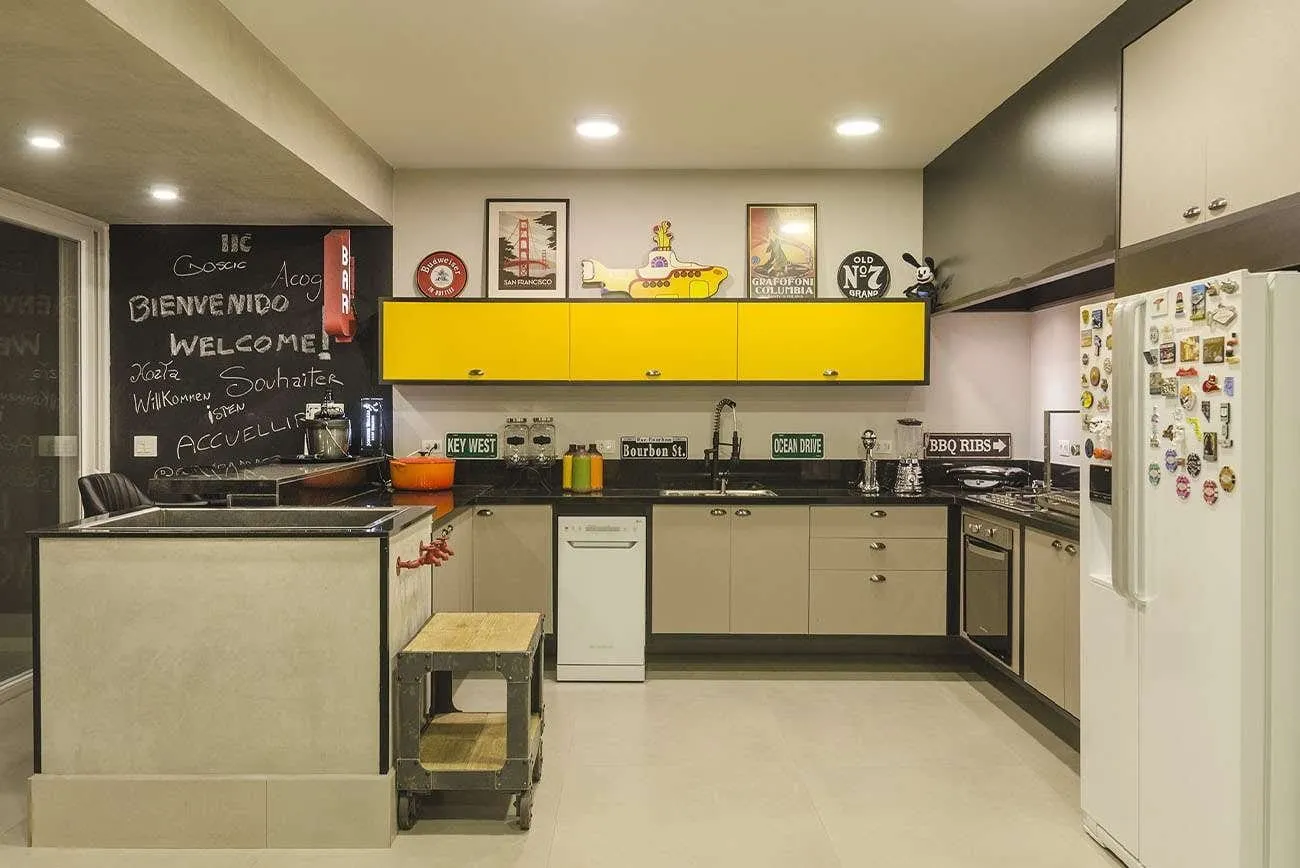 Cozinha planejada com armários amarelos, lousa na parede e geladeira de inox