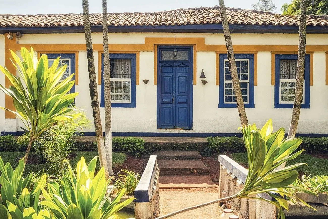 Casa de fachada colonial com portas e janelas azuis e jardim tropical