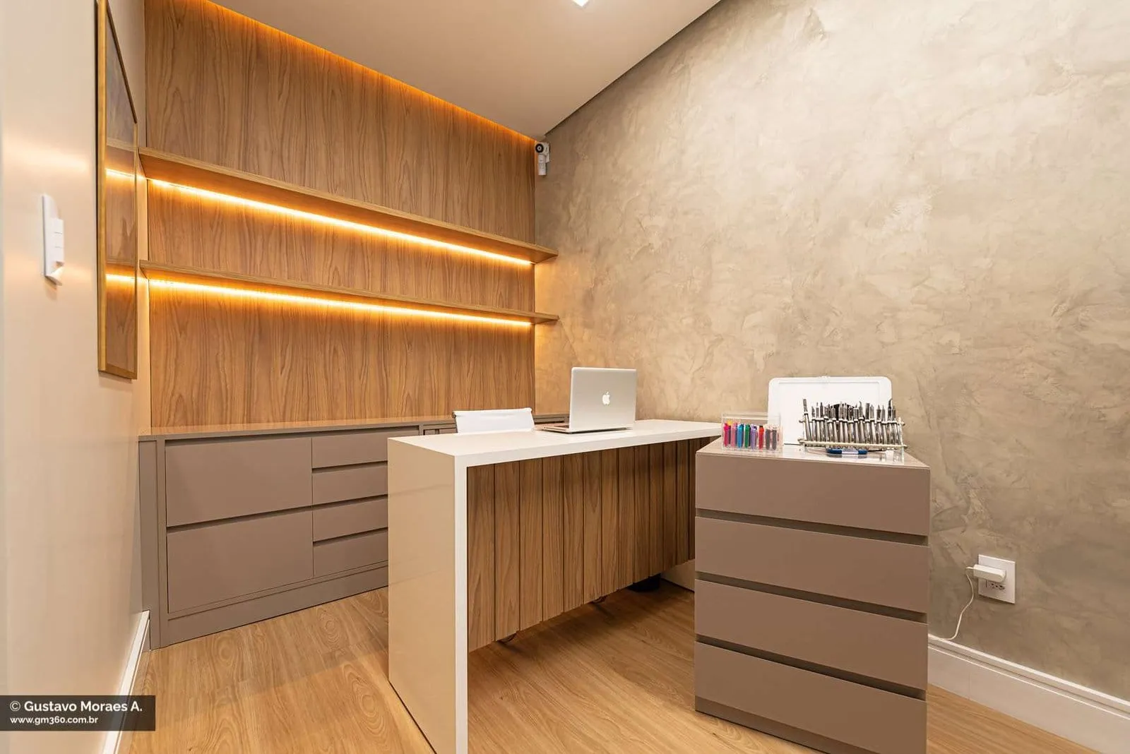 Sala com mesa, gaveteiros e prateleiras de madeira com iluminação embutida