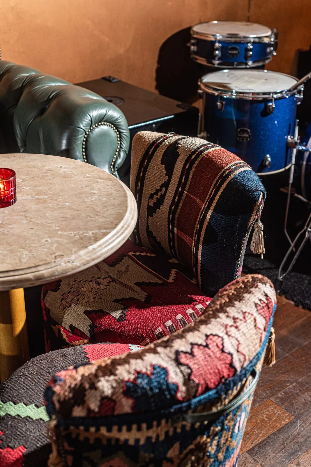 Poltronas forradas de kilim junto a uma mesa de mármore, com sofá de couro verde e bateria ao fundo