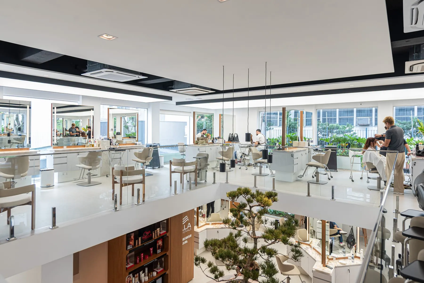 Salão do 1º piso em volta do vão, com bancadas de espelhos, cadeiras de madeira junto ao guarda-corpo de vidro e a copa do Matsu subindo do térreo