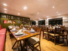 Vista geral do salão da Cantina Castellammare com banco capitonê rosé, parede verde com galeria de fotos, mesas de madeira postas e janelas