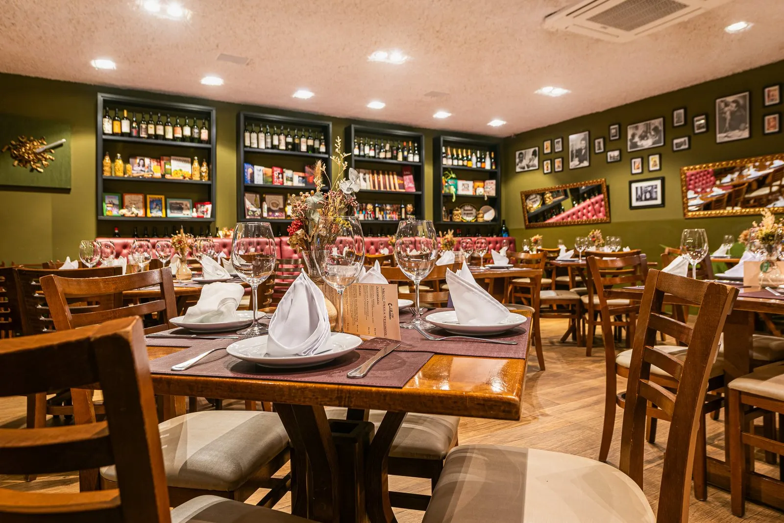 Mesa posta com taças e guardanapos brancos no salão da Cantina Castellammare, em Itapetininga, diante das estantes de vinhos