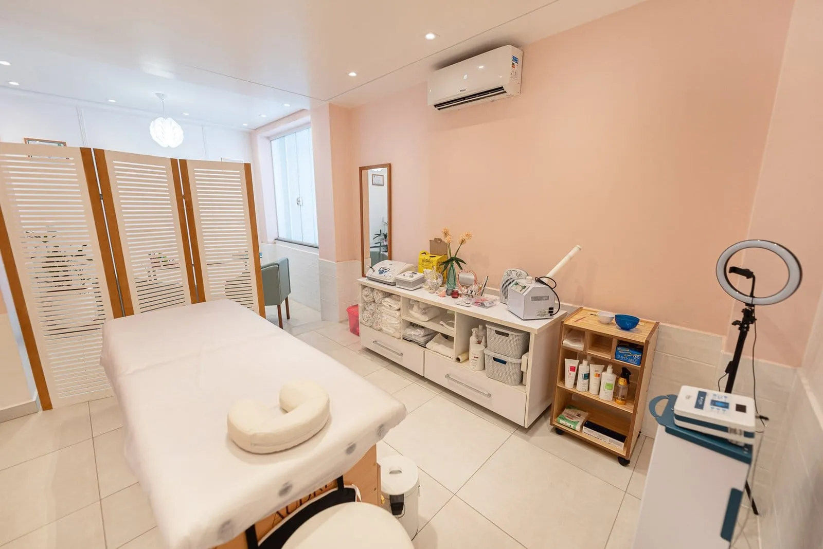 Sala de atendimento com maca, aparelhos de estética, ring light e paredes rosa-claro