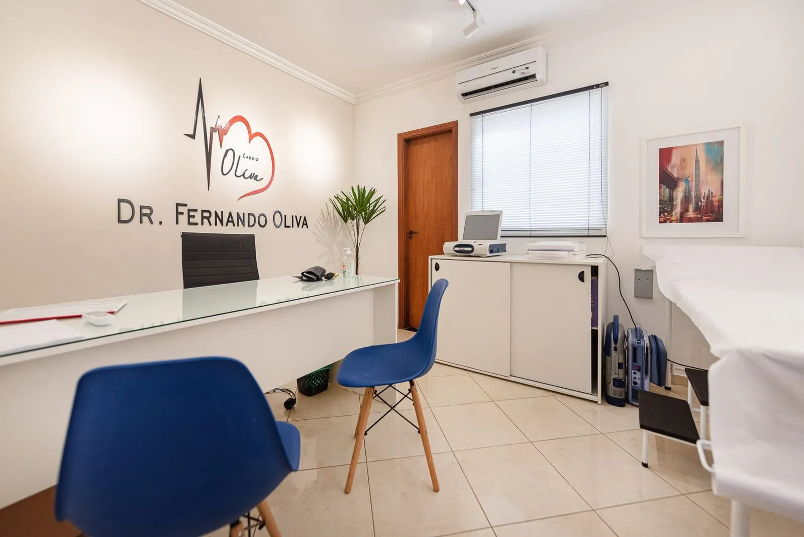 Consultório com mesa branca, cadeira azul e o nome do Dr. Fernando Oliva na parede