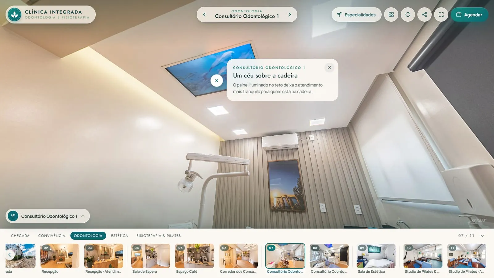 Teto do consultório odontológico 1 no tour, com o painel iluminado que mostra céu e mar azul entre luminárias quadradas e o ponto Um céu sobre a cadeira aberto
