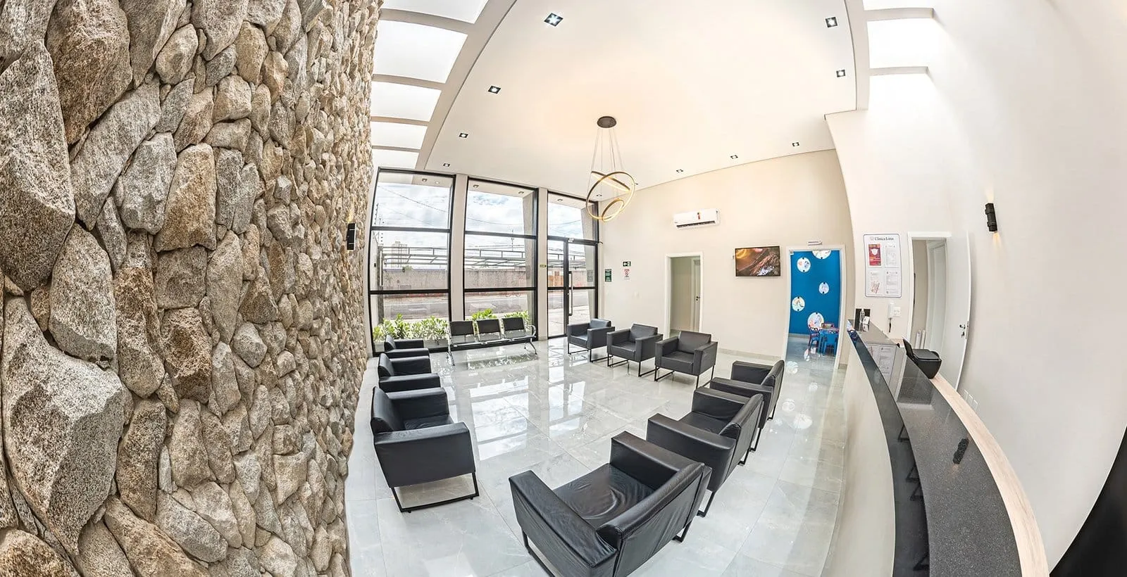 Sala de espera da Clínica Lótus com parede de pedra e poltronas pretas