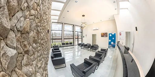 Recepção da Clínica Lótus com poltronas pretas, parede de pedra e janelas amplas ao fundo