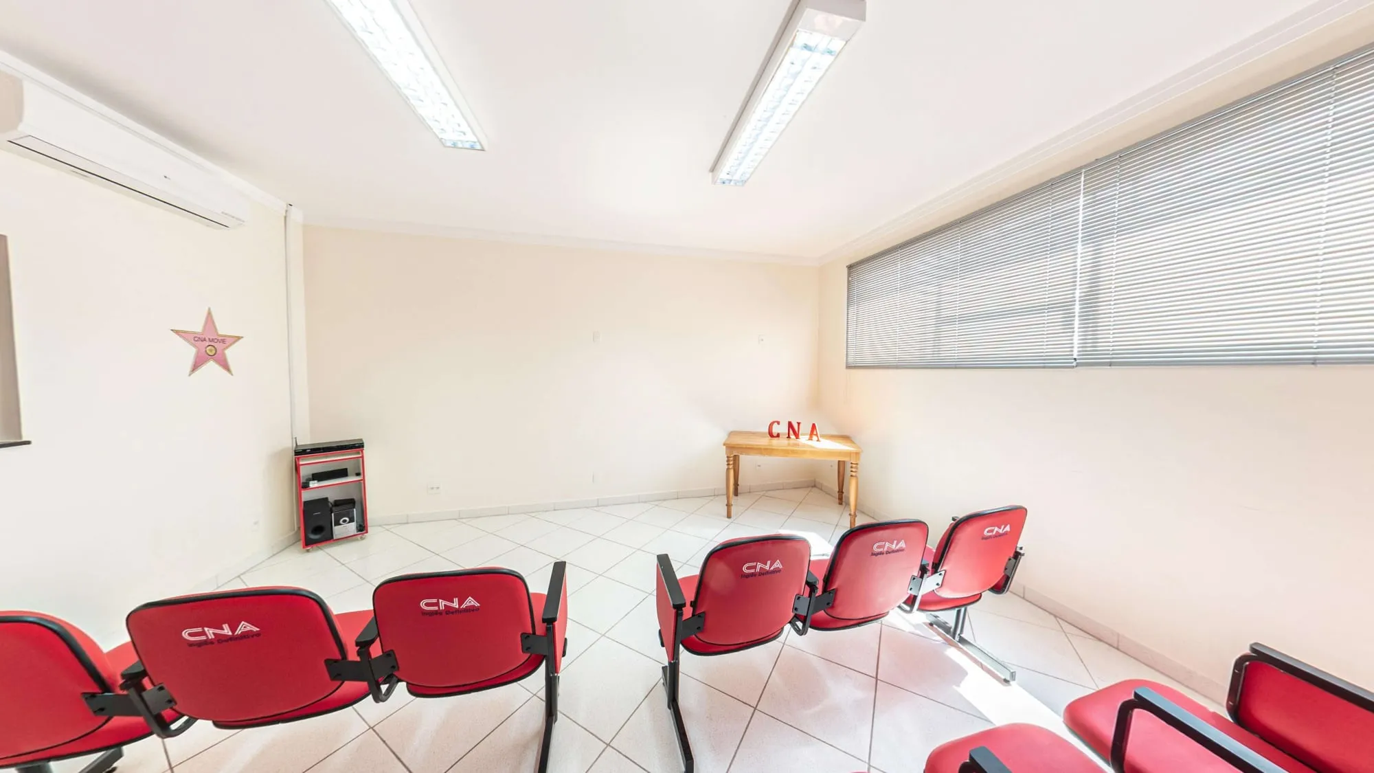Sala de Teatro do CNA Itapetininga, com fileiras de cadeiras vermelhas com a marca CNA voltadas para o palco