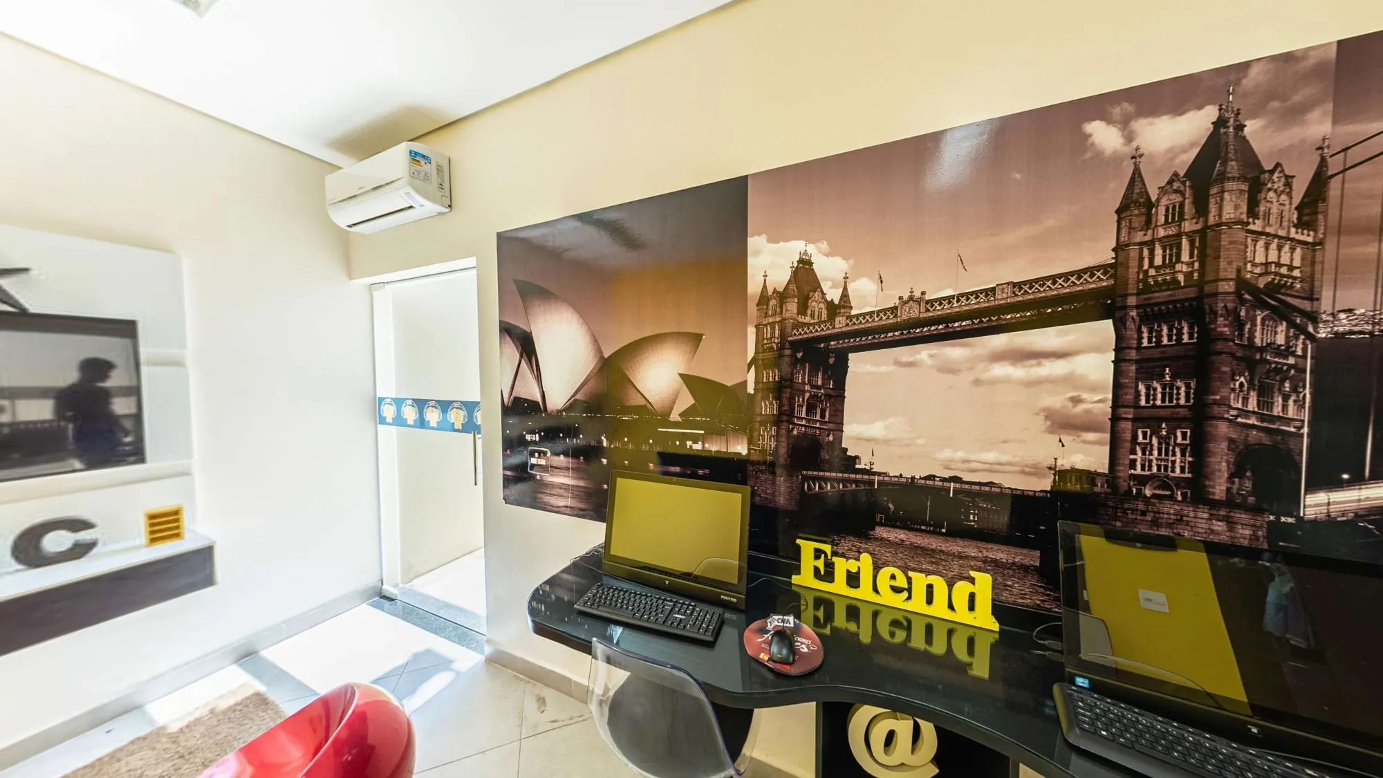 Sala Música do CNA Itapetininga, com painel da Tower Bridge, notebooks em mesa preta e puffs vermelhos