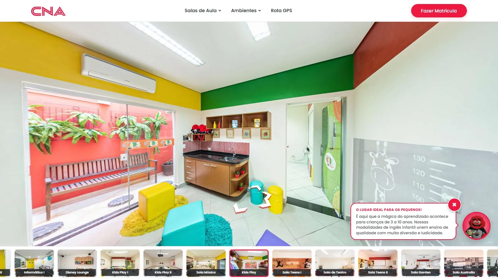 Sala Kids Play no tour, de paredes amarela, verde e vermelha, com o mascote vermelho e o balão O lugar ideal para os pequenos!, sobre o inglês para crianças de 3 a 10 anos