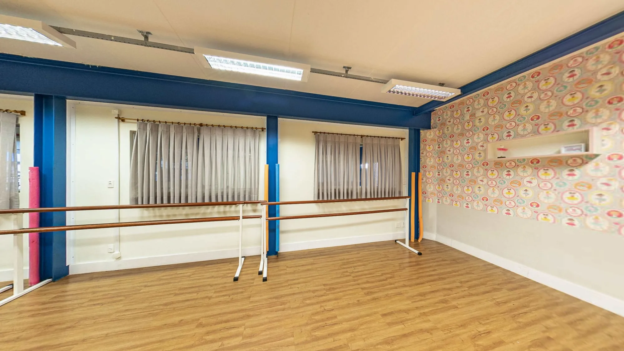Sala de ballet do Colégio Alpis Veredas, com barras de madeira, piso de madeira, papel de parede com bailarinas e espelhos
