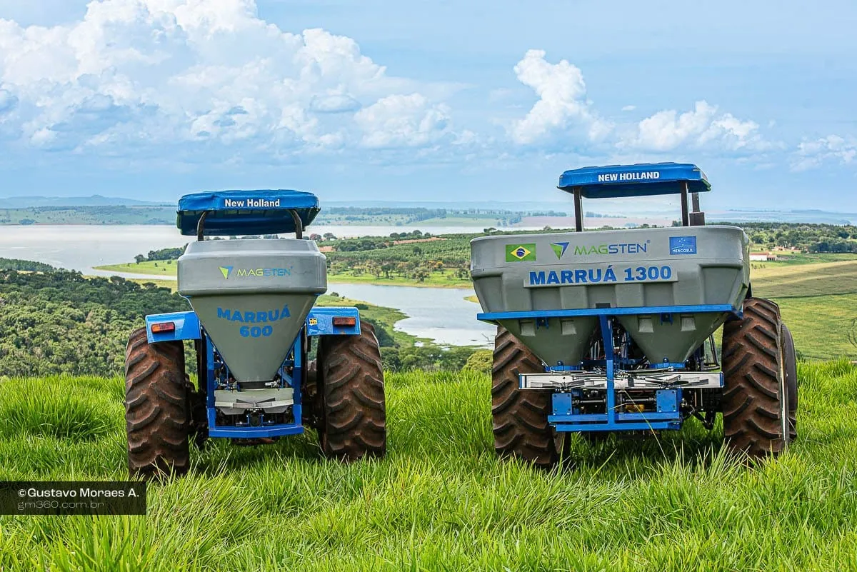 Distribuidores Magsten Marruá 600 e 1300 montados em tratores, lado a lado no pasto, com um lago ao fundo