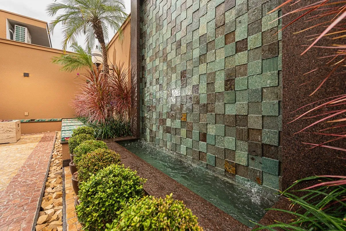Parede de cascata revestida em peças de rocha verde, com jardim de buxinhos e canteiro de seixos