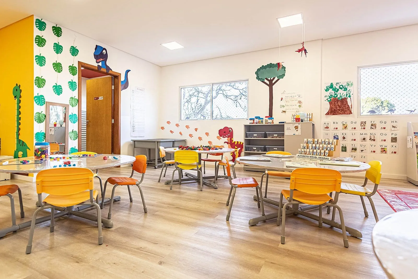 Sala de aula da Maple Bear Itapetininga com mesas, cadeiras amarelas e laranja e paredes decoradas com árvores