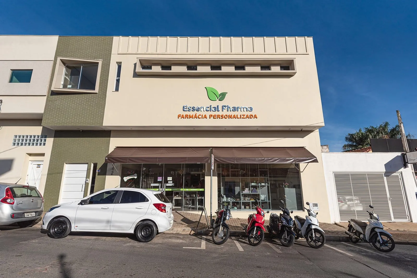 Fachada da Essencial Pharma em Itapetininga, com motos e um carro estacionados em frente