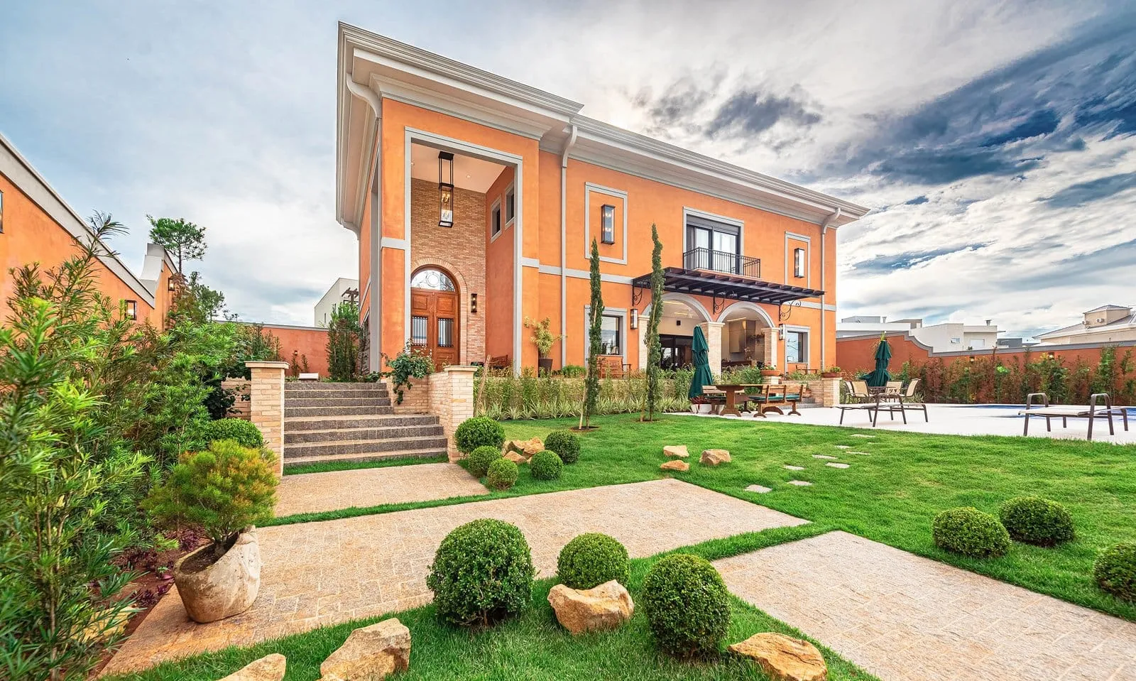 Casa de fachada em tons de terracota com escada de pedra, jardim e gramado