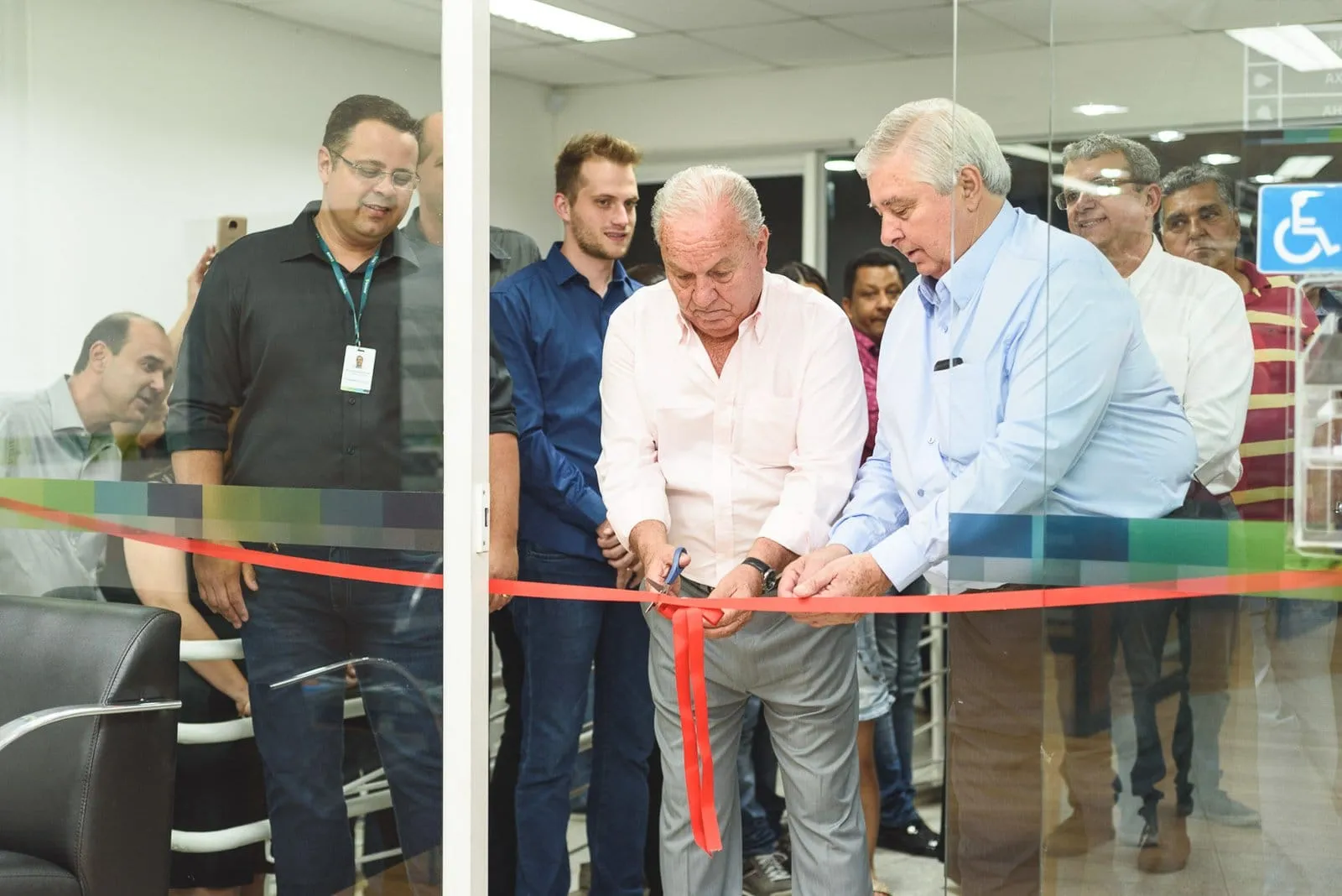 Corte da fita vermelha na inauguração de uma agência, com convidados ao redor