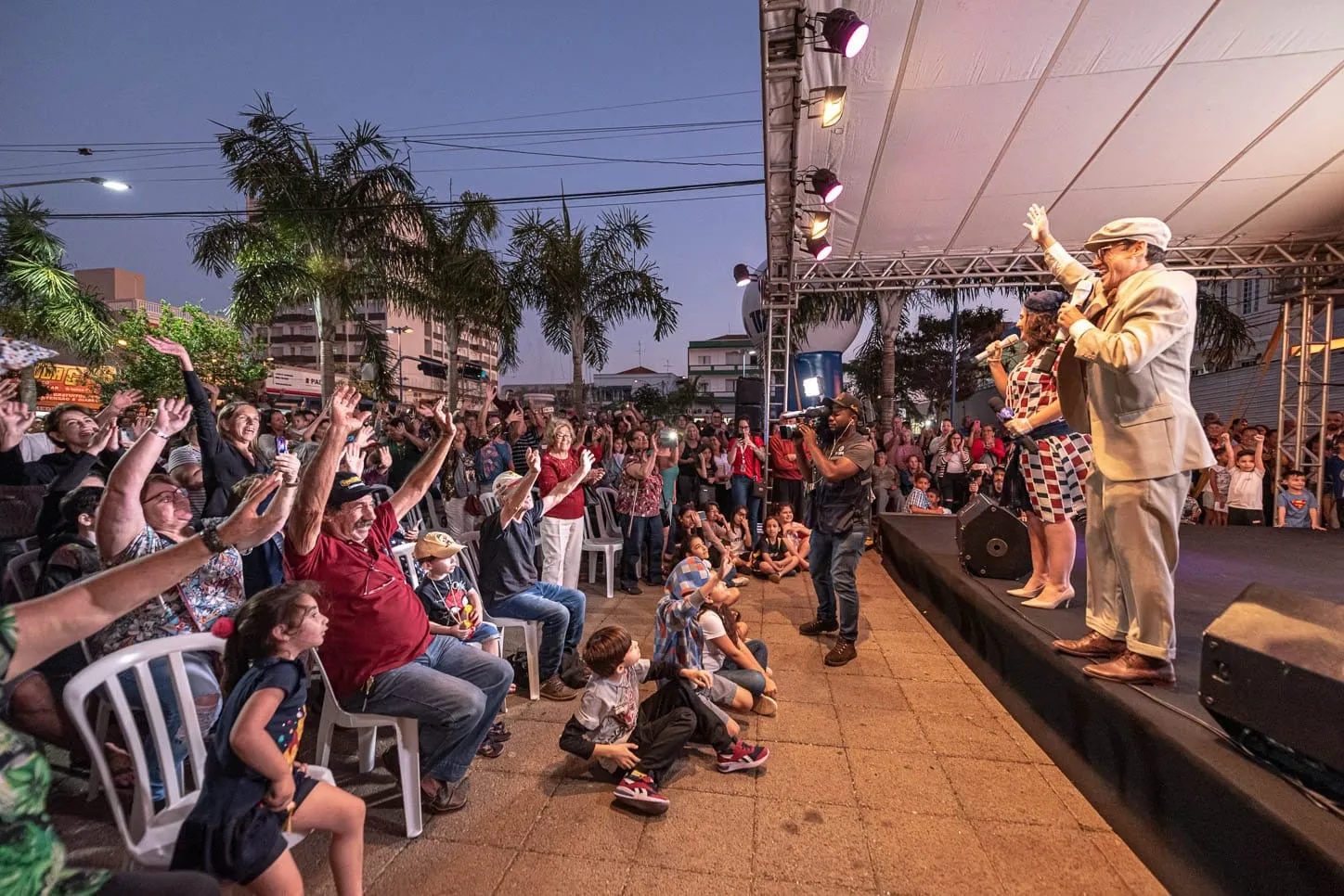 Público de braços erguidos diante de um palco montado na rua, ao entardecer