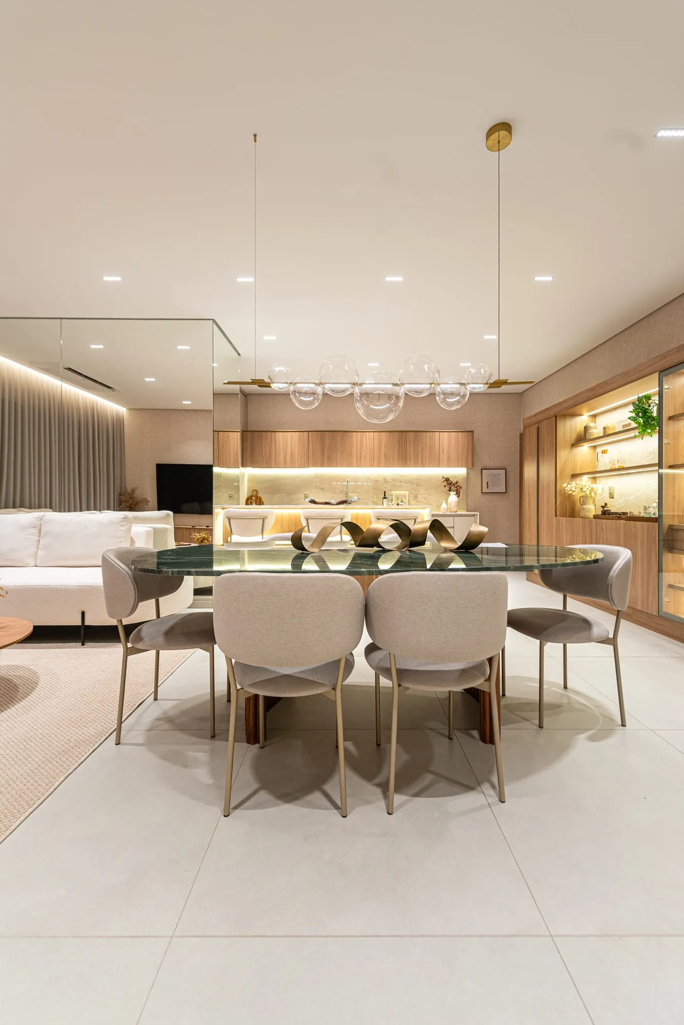 Vista frontal da mesa de jantar com seis cadeiras, tendo ao fundo a sala de estar e a cozinha integradas