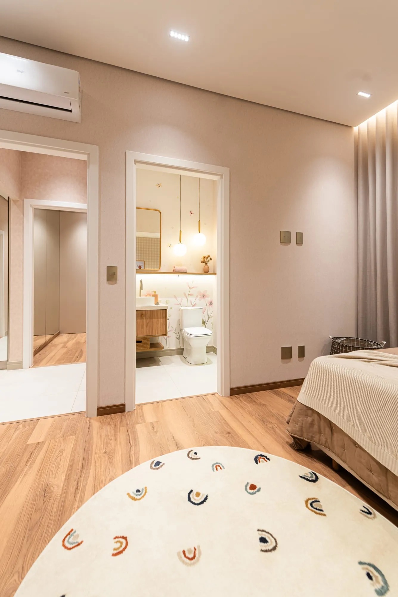 Suíte 2 com piso laminado e tapete redondo, vista para o banho privativo e para o hall íntimo pelas portas