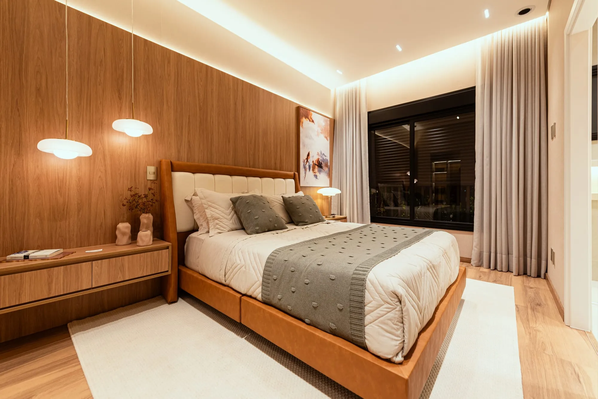 Suíte master do decorado Grand'Oro Vila Barth com painel de madeira, cabeceira em couro caramelo e janela ampla