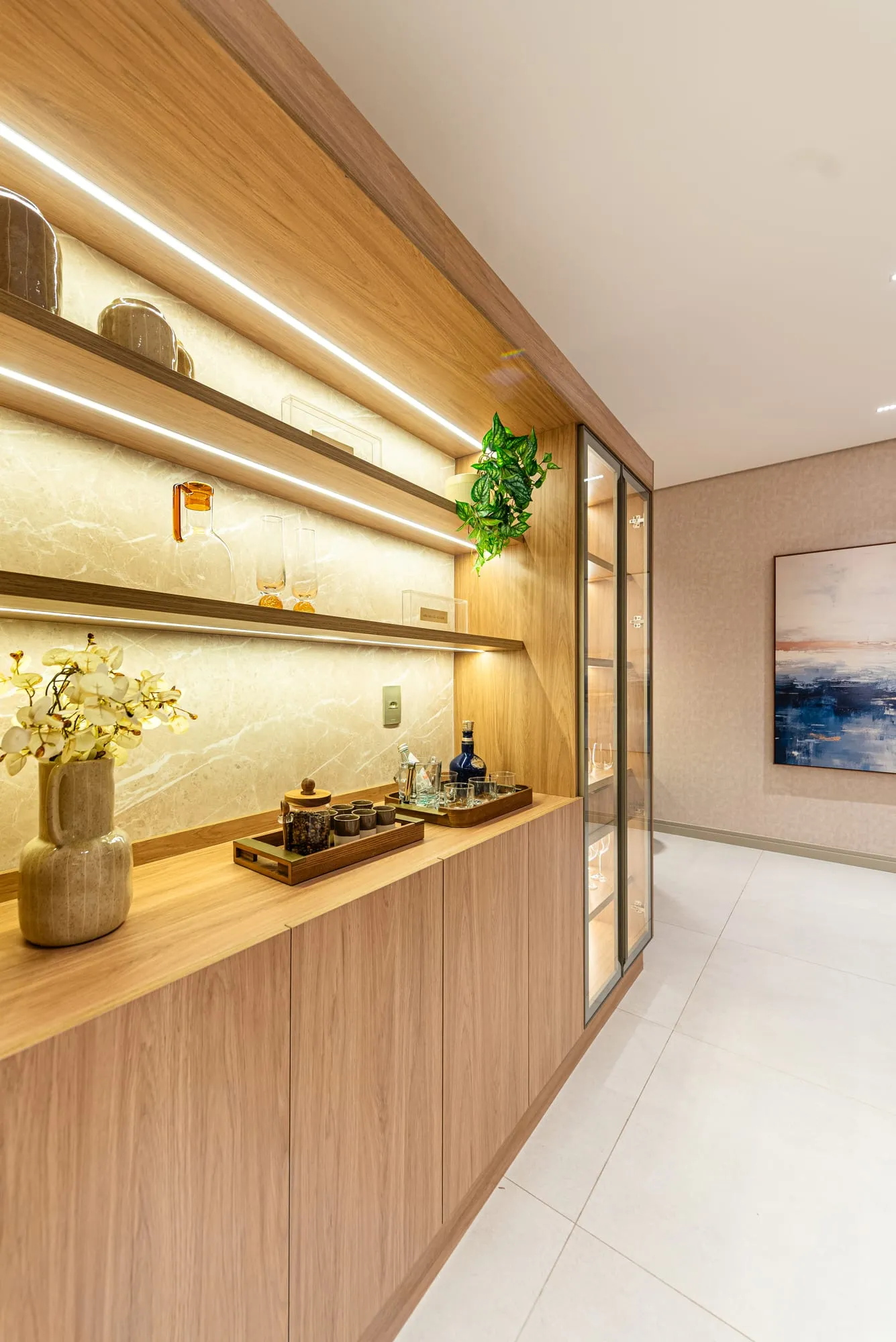Aparador iluminado com prateleiras, orquídea e objetos decorativos junto à cristaleira da sala