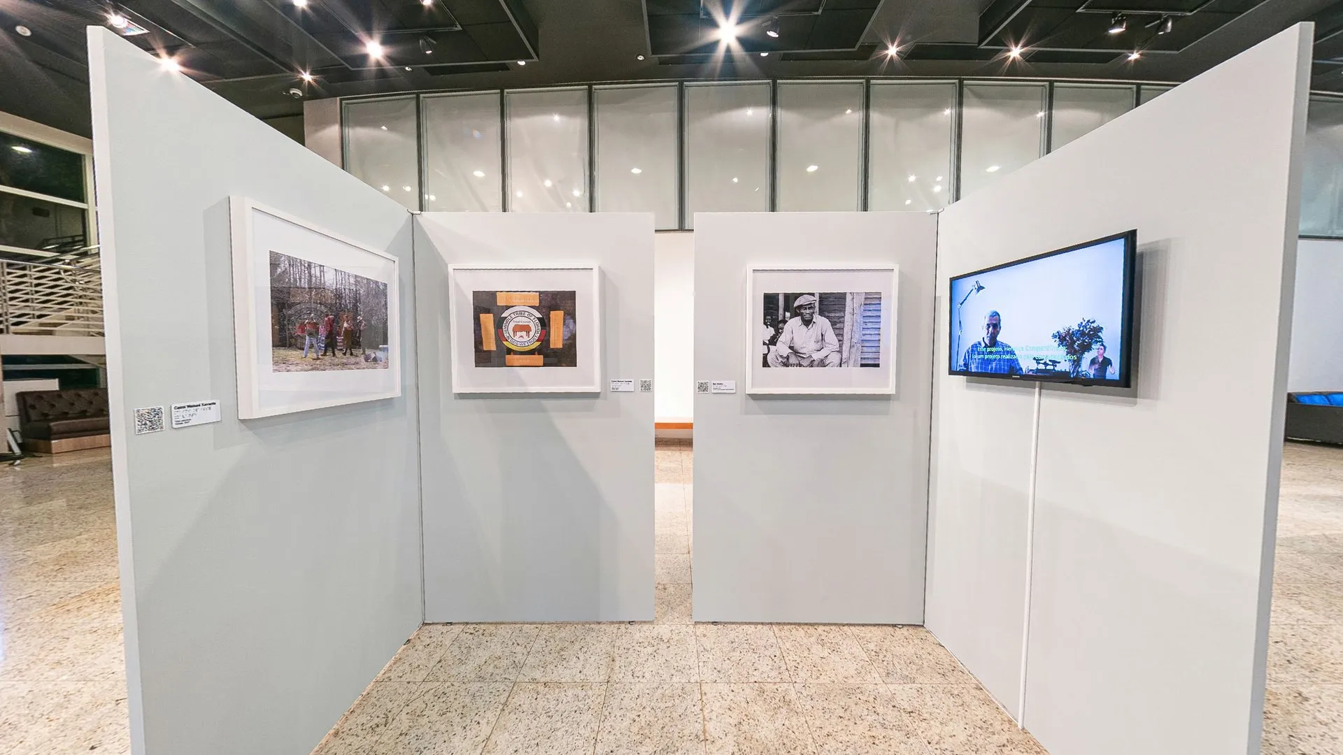 Biombos da exposição Herança Compartilhada com fotografias emolduradas e um monitor de vídeo, no Foyer do Teatro do SESI Itapetininga