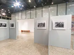 Biombos cinza da exposição Herança Compartilhada no Foyer do Teatro do SESI Itapetininga, com fotografias emolduradas e o banner da mostra ao fundo
