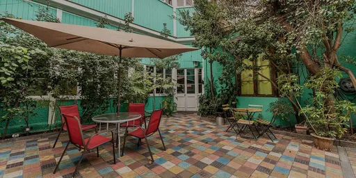 Pátio interno do Hostal Providencia com piso colorido, guarda-sol, cadeiras vermelhas e muitas plantas