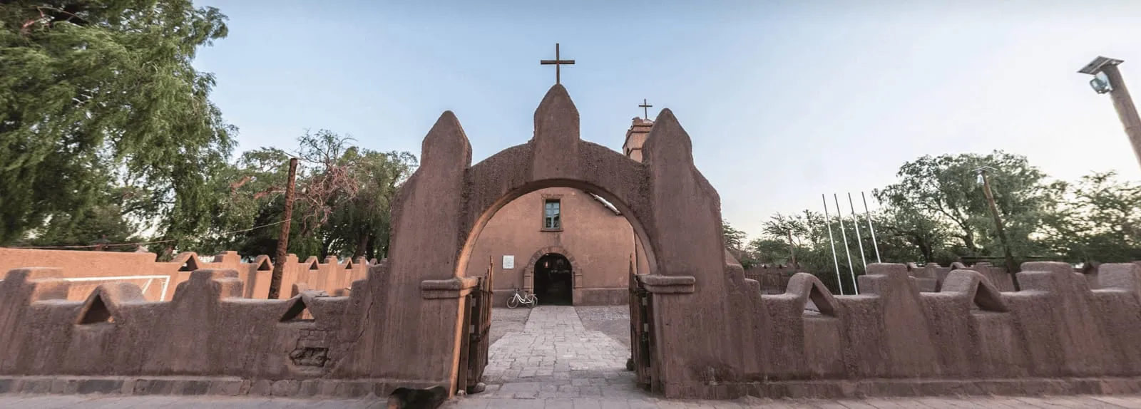 Portão em arco no muro de terra da Iglesia de San Pedro, com a fachada da igreja e o campanário ao fundo