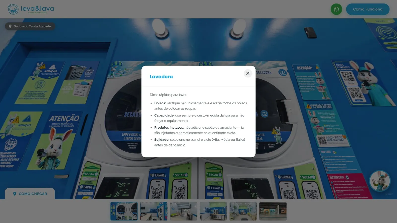 Janela Lavadora aberta no tour 360° da Leva & Lava, com as dicas rápidas para lavar (bolsos, capacidade, produtos inclusos e sujidade) por cima das secadoras empilhadas sobre as lavadoras e dos cartazes de instrução da loja