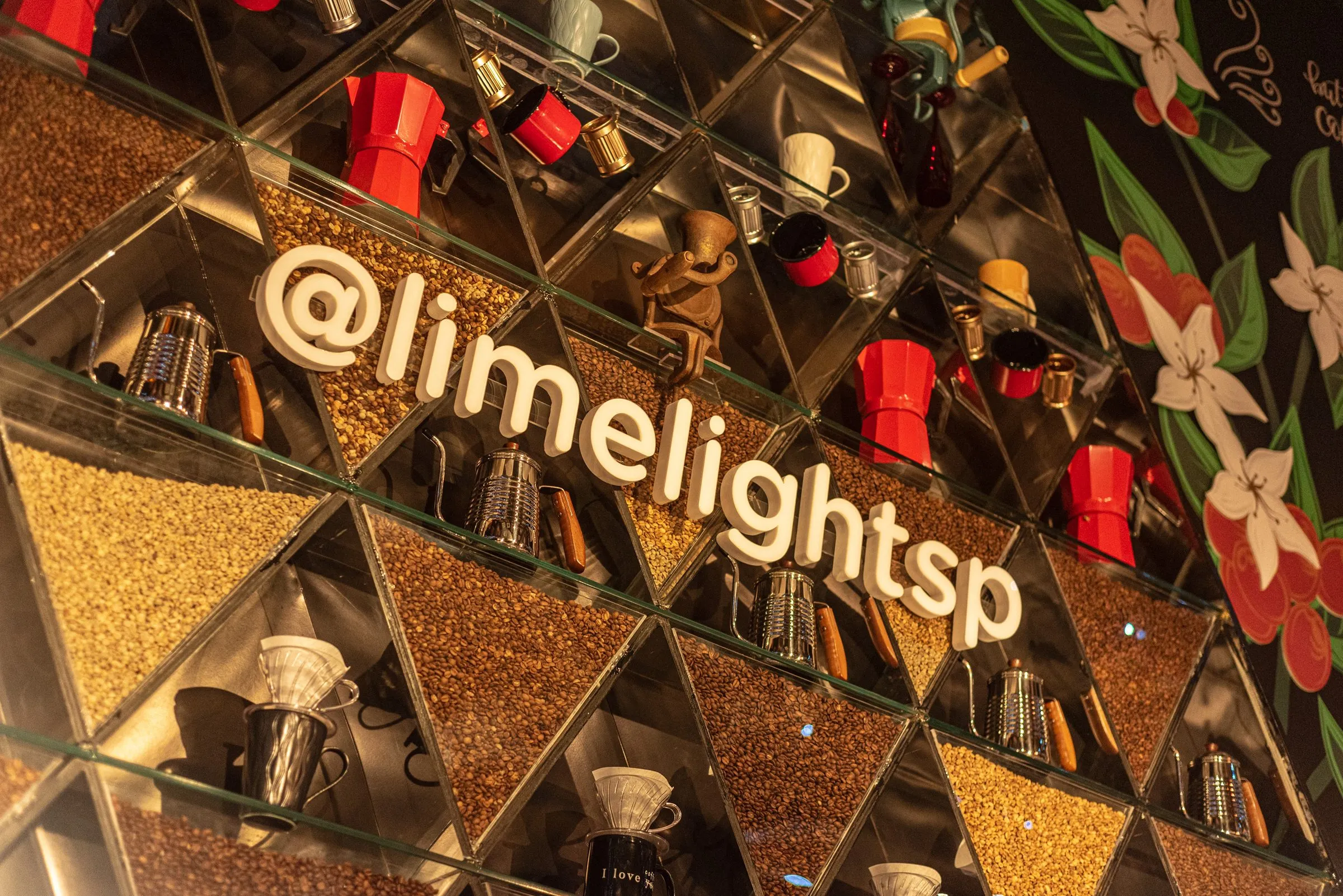 Detalhe da estante triangular do Bar Café, com nichos de grãos de café, cafeteiras vermelhas, chaleiras e o letreiro @limelightsp