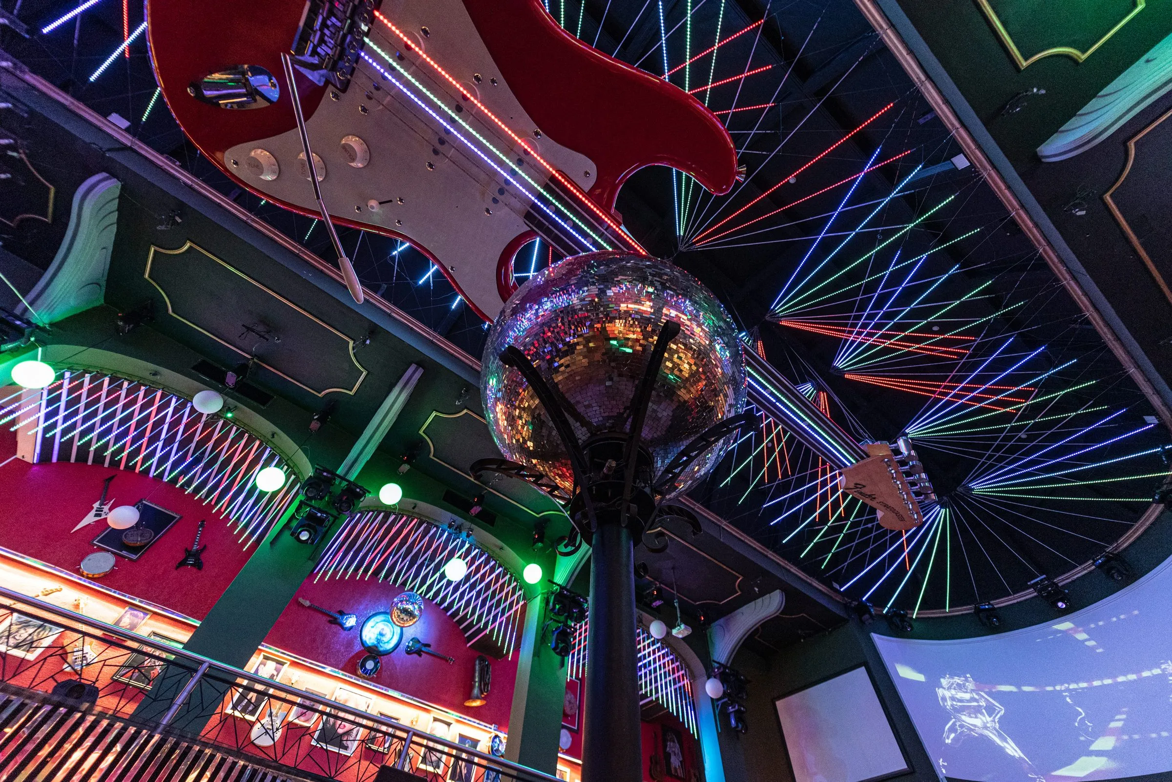Teto da pista da Limelight visto de baixo, com uma guitarra vermelha gigante suspensa, o globo espelhado no alto da coluna, linhas de luz coloridas em leque e os mezaninos de paredes vermelhas com guitarras penduradas