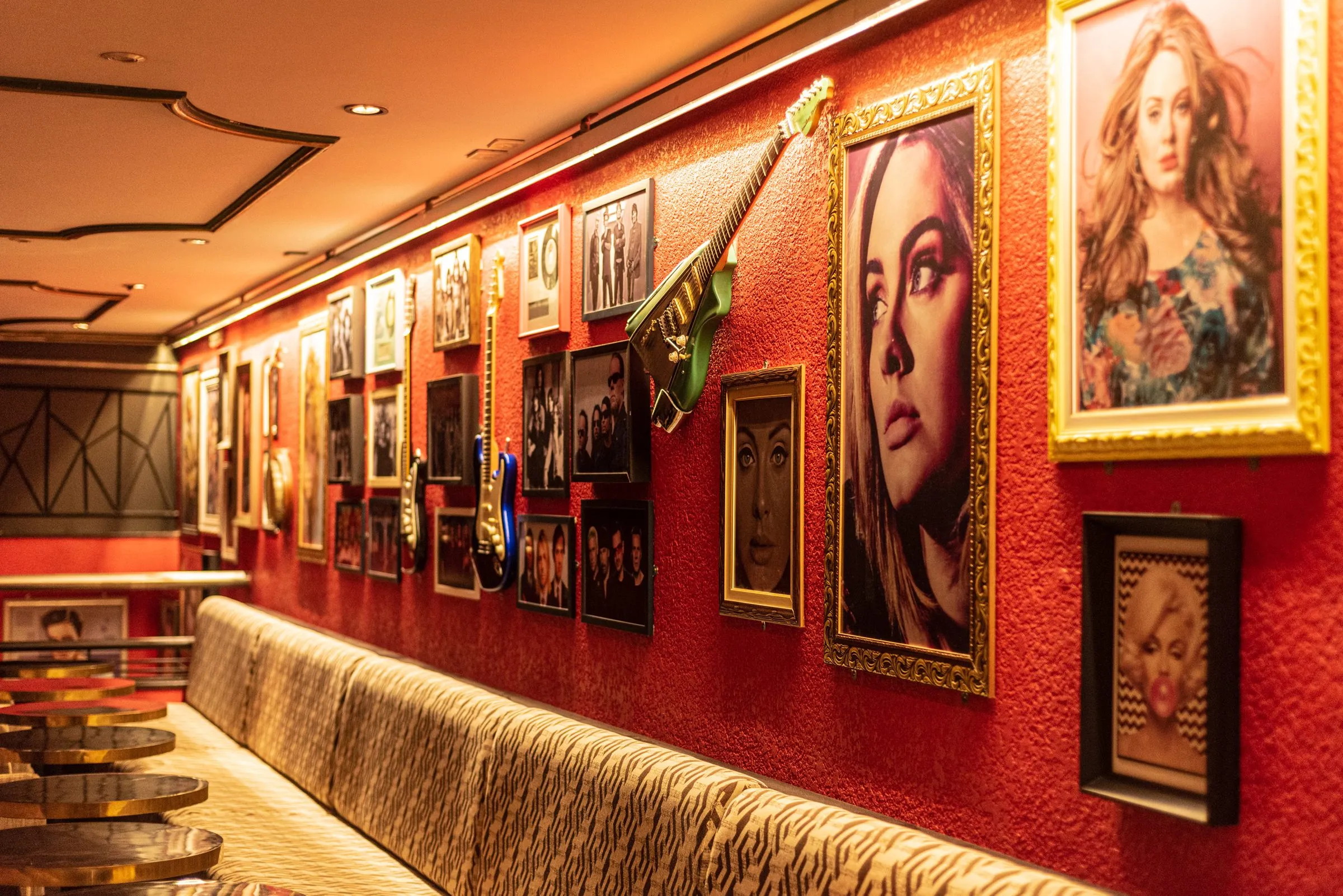 Lounge da Limelight com sofá comprido de estampa de zebra junto à parede vermelha, coberta de retratos de cantoras em molduras douradas, fotos de bandas em preto e branco e guitarras penduradas
