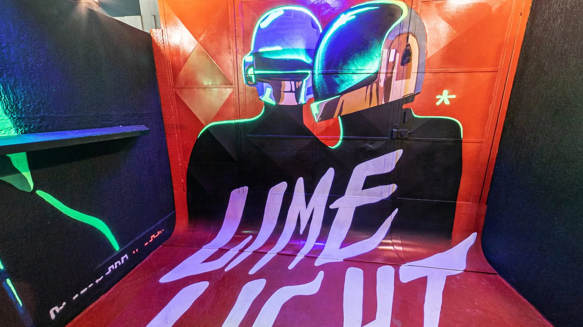 Mural do fumódromo da Limelight, com duas figuras de capacete contornadas em neon verde sobre fundo laranja e o nome Limelight pintado em letras brancas no chão