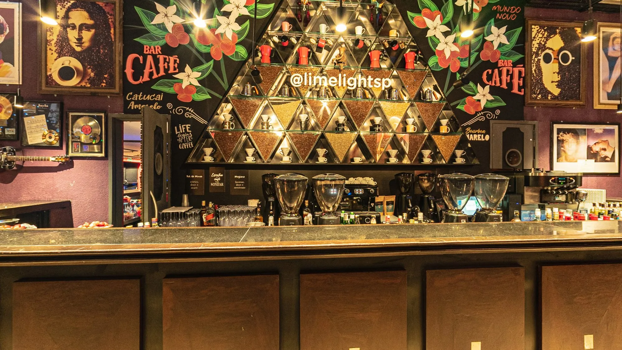 Bar Café no hall de entrada da Limelight, com o balcão, a estante triangular de cafés e xícaras, o @limelightsp em letras de luz, pinturas de flores de café e quadros de ídolos da música na parede