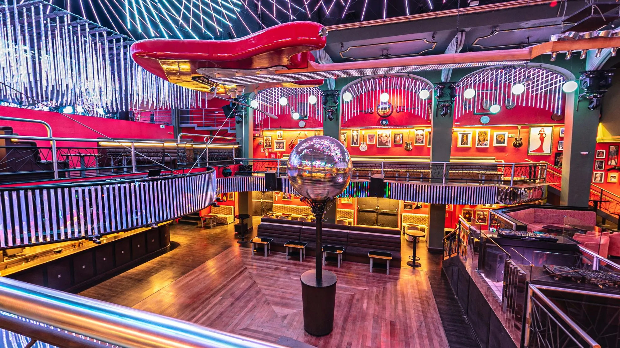 Pista da Limelight vista do mezanino, com uma guitarra vermelha gigante pendurada sob a cortina de tubos de LED, o globo espelhado no centro, sofás, a cabine do DJ à direita e paredes vermelhas com quadros e guitarras