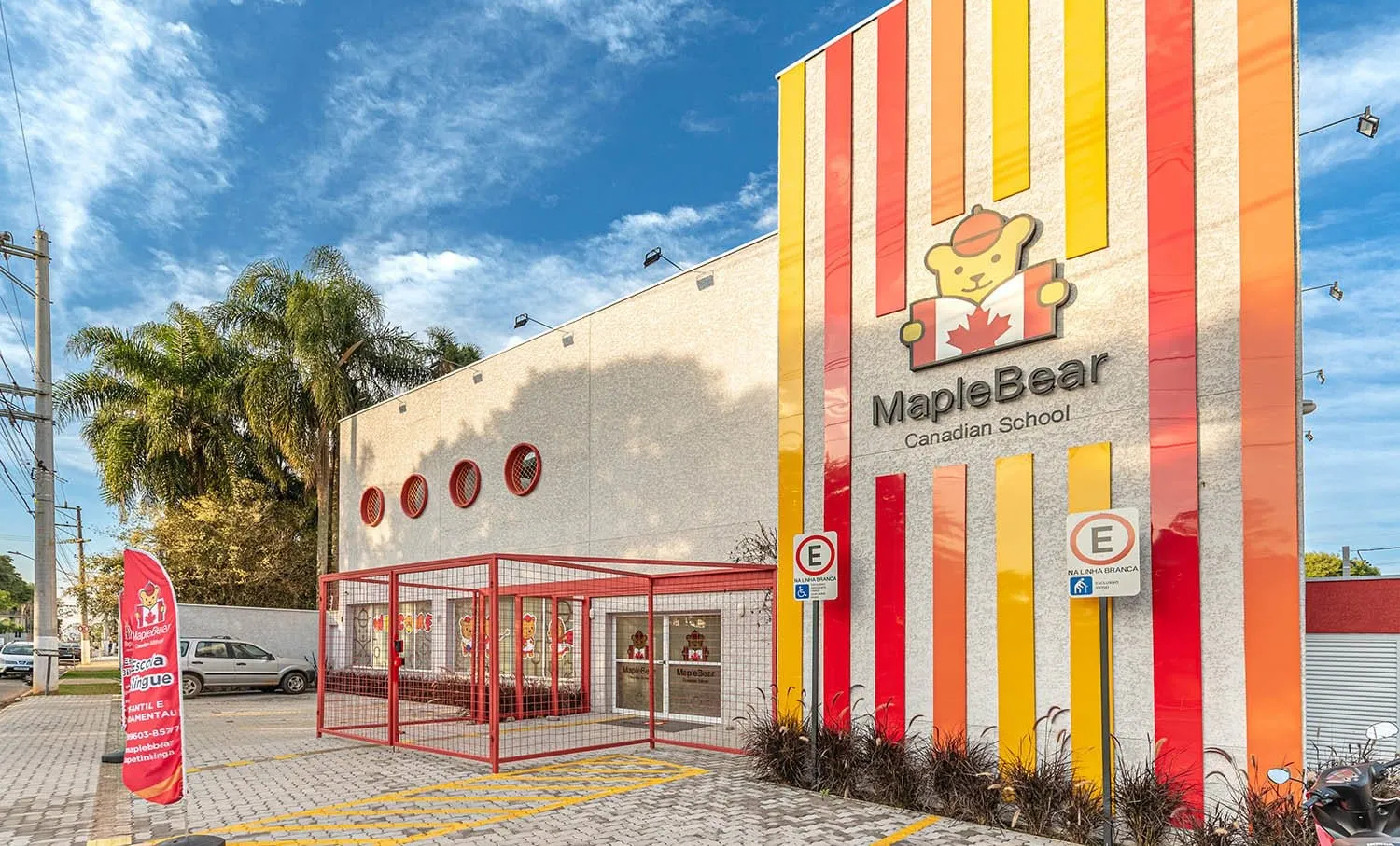 Fachada da Maple Bear Itapetininga com faixas verticais vermelhas, laranja e amarelas e o logotipo da escola