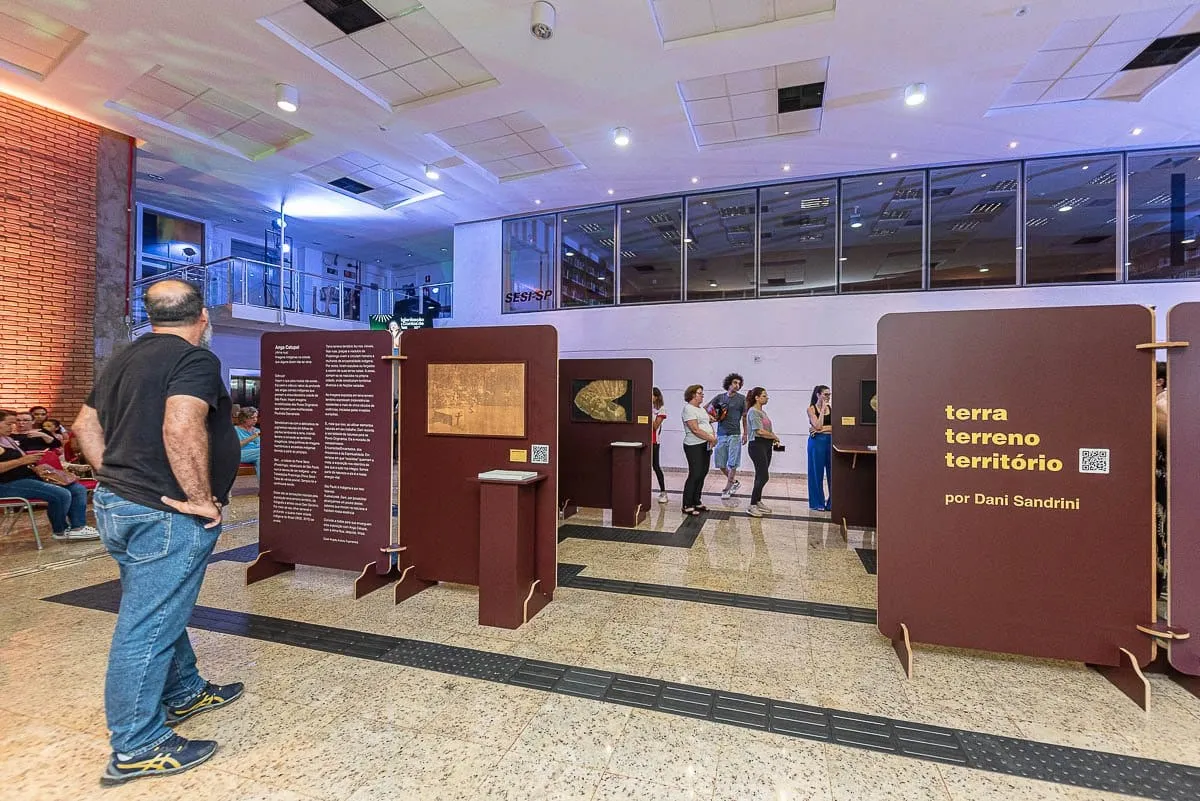 Painéis bordô da exposição montados no saguão, com o painel de título Terra Terreno Território por Dani Sandrini