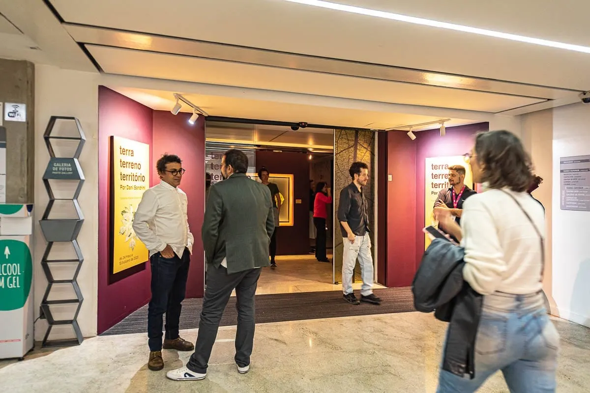 Entrada da exposição Terra Terreno Território na galeria de fotos da FIESP, com cartaz da mostra e visitantes na porta