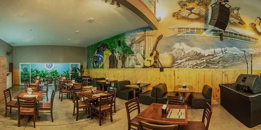 Salão do Posto 1 Pub com mesas de madeira, poltronas e um grande painel pintado na parede