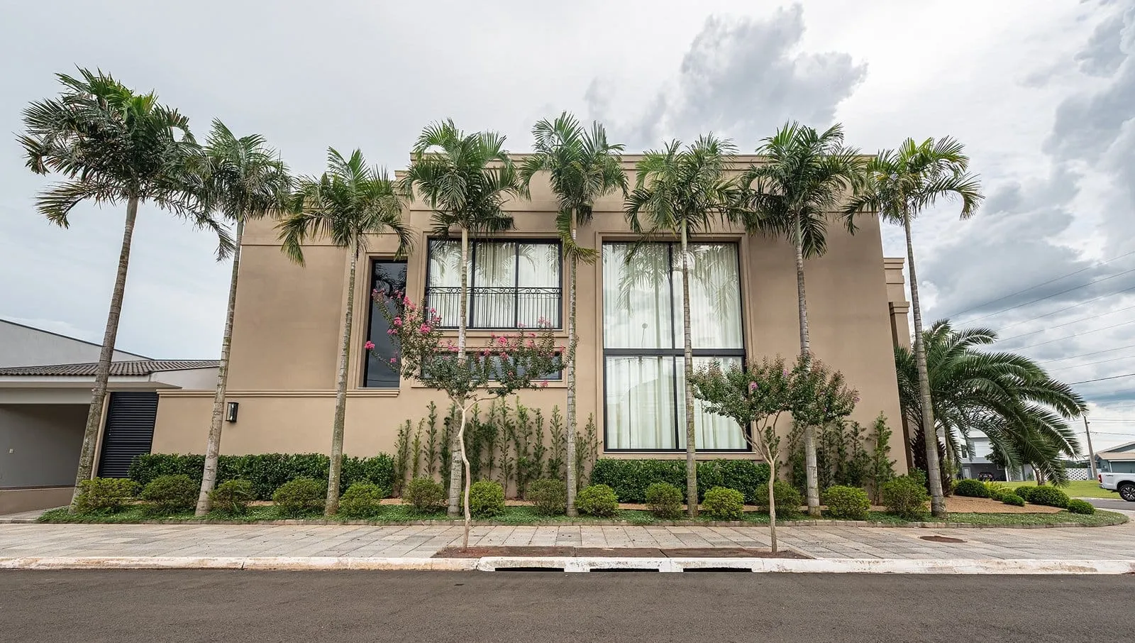 Fachada lateral da Residência R&M com janelas altas e fileira de palmeiras