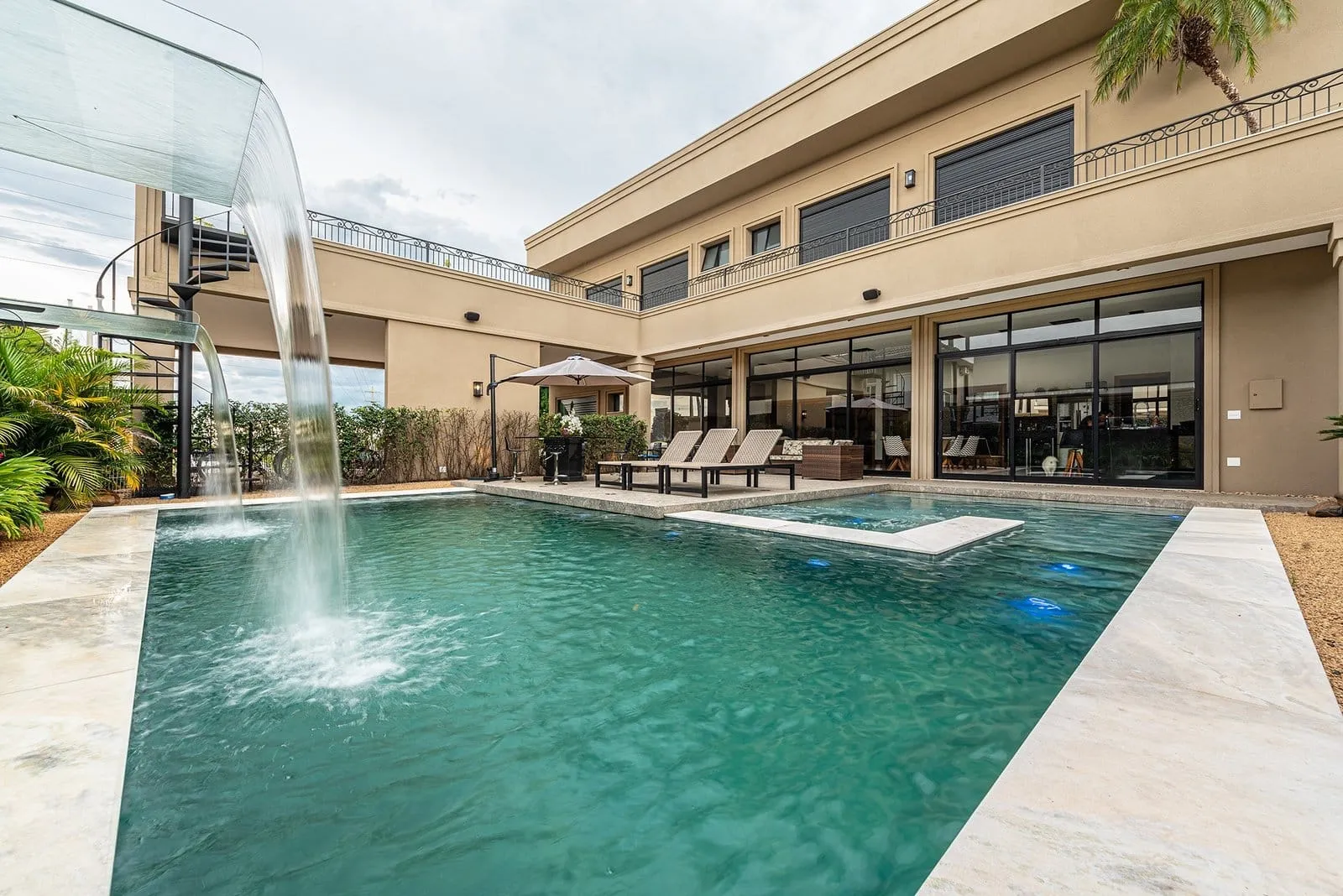 Cascata caindo na piscina da Residência R&M, com a fachada envidraçada ao fundo