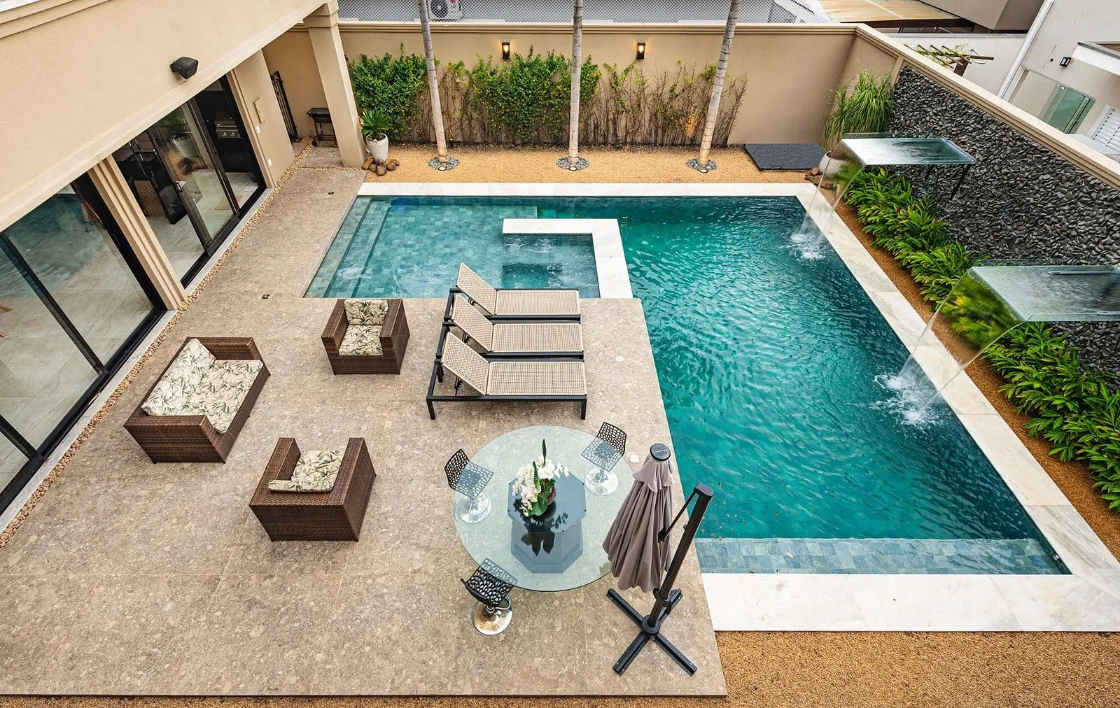 Área da piscina da Residência R&M vista do andar de cima, com mesa, poltronas e jardim
